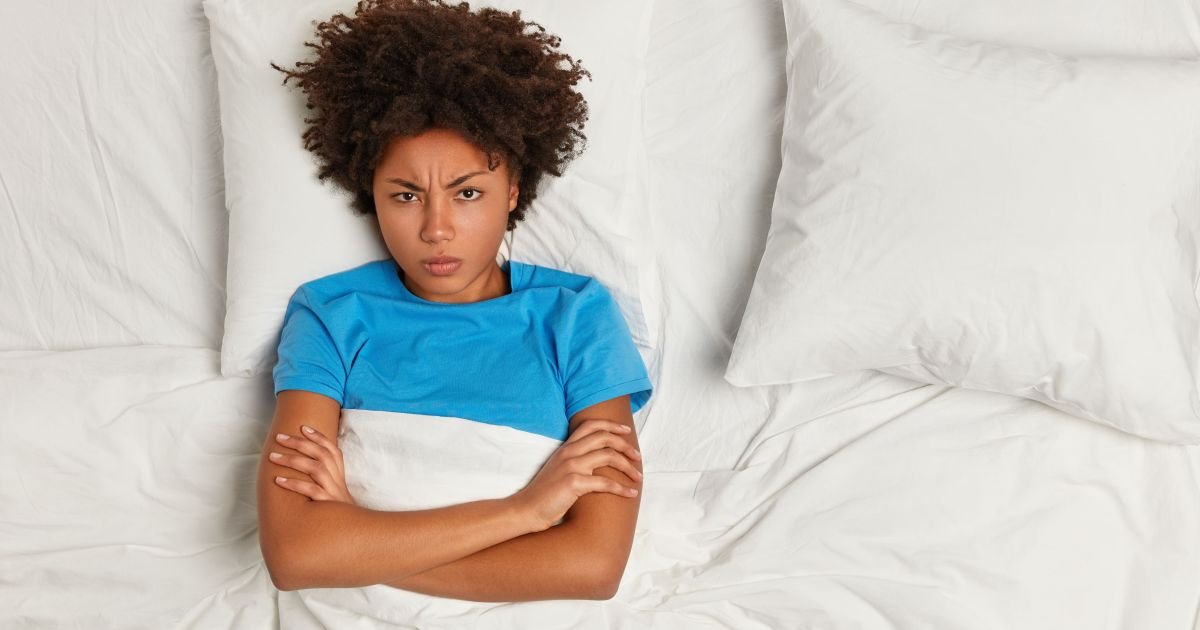 Mulher-negra-de-cabelo-curto-cacheado-esta-deitada-numa-cama-branca-de-bracos-cruzados-sobre-a-cober.jpeg